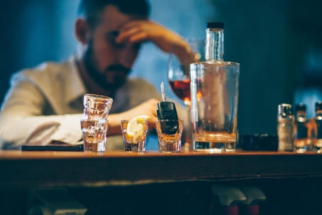 man sitting at a bar alone with shots of alcohol and car keys in front of him