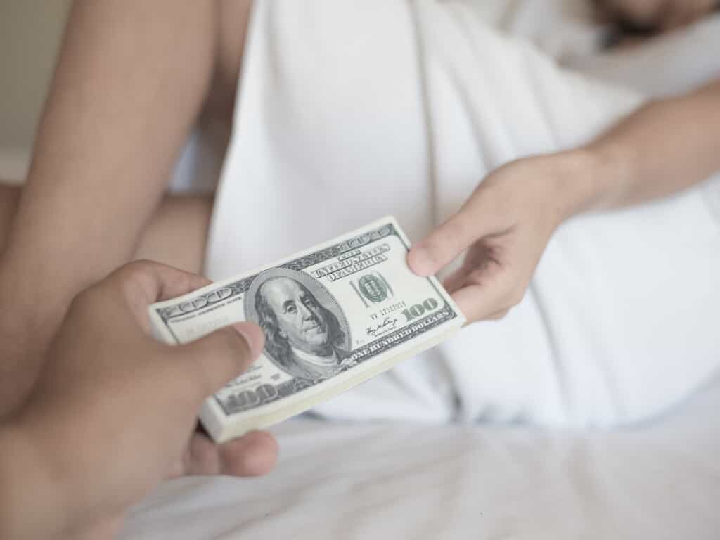 Two Individuals Exchanging Money in Bed